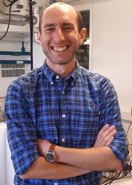 Headshot of Chris Mark who is bald and is wearing a dark, plaid, collared shirt.