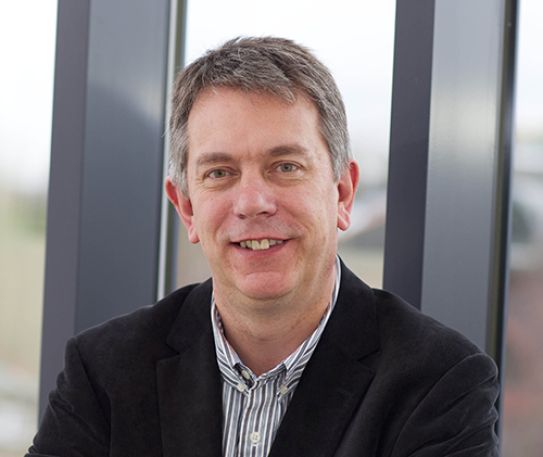 Headshot of Dr Michael Simmons who has short hair and is wearing light collared shirt and dark jacket.